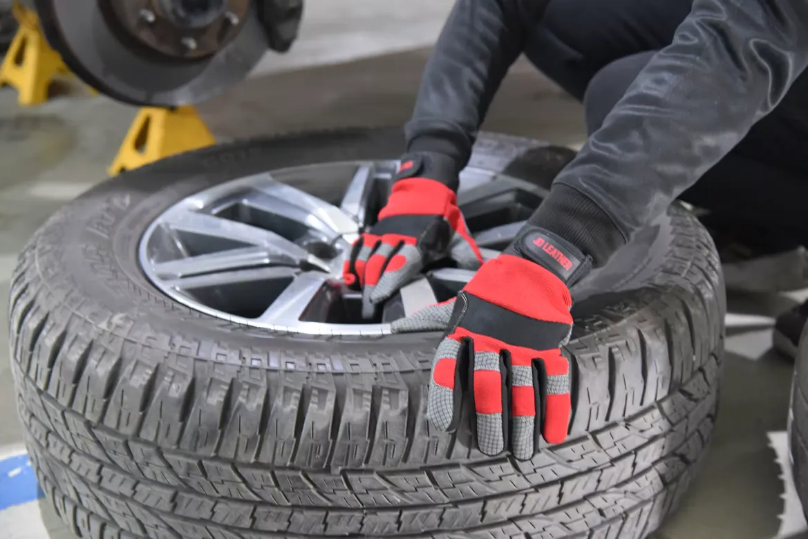 Hände in Werkstatthandschuhen montieren ein Rad mit Alufelge